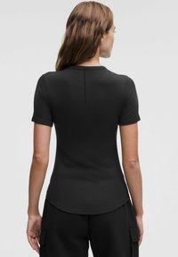 Tricou negru cu mânecă scurtă, cu un tiv rotunjit, textură fină și un detaliu subtil al cusăturii pe spate. Asortat cu pantaloni largi negri.