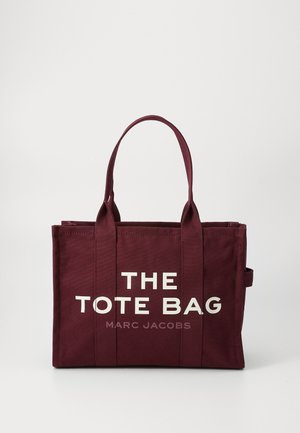 Burgunderfarget canvas tote bag med to bærehåndtak, med stor hvit tekst som sier "THE TOTE BAG" og mindre tekst "MARC JACOBS" under.