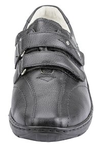 Zwart leren casual schoen met dubbele klittenbandsluitingen, gestructureerde afwerking en gevoerde witte binnenvoering die zichtbaar is bij de hak.