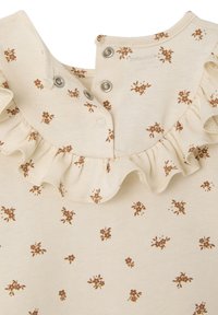 Cream-colored fabric featuring a floral print in brown. Ruffled collar with snap closures at the back. Soft texture, casual design.