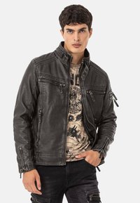 Schwarze Lederjacke mit Stehkragen, mehreren Reißverschlusstaschen und strukturiertem Finish, getragen über einem Grafik-T-Shirt.