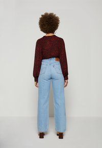 Blusa longa de mangas bufantes com padrão em bordeaux, combinada com jeans de perna larga de cintura alta em azul claro, apresentando uma etiqueta de couro na cintura.