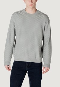 Lichtgrijze sweatshirt met een gestructureerd ruitpatroon, ronde halslijn en geribbelde boorden en zoom. Gedragen over donkere jeans.