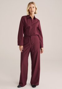 Burgundská košile na knoflíky s dlouhými rukávy a límečkem, v kombinaci se širokými kalhotami s vysokým pasem ve stejné barvě. Hladká textura, minimalistic design.