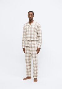 Pánsky pyžamový set s károvaným vzorom v béžových odtieňoch. Vrchný diel má golier a gombíky, nohavice majú elastický pás. Pohodlná látka.