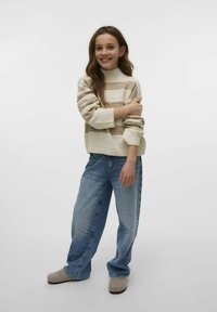 Pleteni krem pulover z bež črtami, kroja z okroglim izrezom in z ribastimi manšetami, v kombinaciji s širokimi svetlo modrimi jeans hlačami in sivimi natikači.