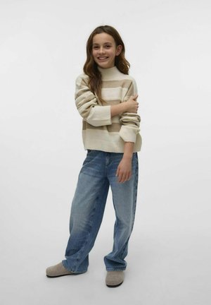 Pull en crème tricoté avec des rayures beiges, col rond et poignets côtelés, associé à un pantalon large en jean bleu clair et des chaussures slip-on grises.