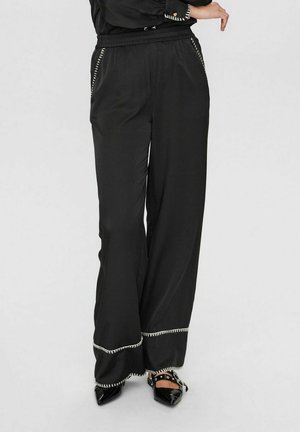 Pantaloni neri a gamba larga realizzati in tessuto liscio, dotati di una cintura elasticizzata e cuciture bianche a contrasto lungo l'orlo e le tasche.