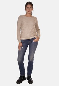 Suéter de punto beige con un patrón ondulado texturizado, cuello redondo y mangas largas; combinado con jeans azul oscuro y botas negras de cordones.