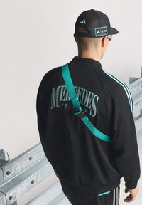 Czarna sportowa kurtka z turkusowymi pasami i logo, połączona z czapką w kolorze czarnym z turkusowym akcentem i regulowanym zapięciem.