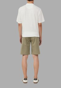 Weißes gestricktes Kurzarmoberteil mit subtiler Textur, kombiniert mit olivgrünen Shorts. Die Schuhe haben eine weiße Basis mit schwarzen Akzenten.