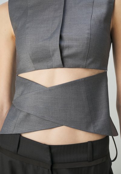 Gray sleeveless top with cutout design, featuring sharp geometric lines and a textured fabric; paired with black tailored pants.