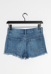 Pantalones cortos de mezclilla con dobladillo deshilachado, color azul claro, dos bolsillos traseros y un diseño clásico de cinturilla, exhibidos en un gancho negro.