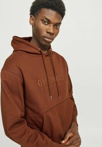 Brun hætte sweatshirt med et præget logo, frontlomme, justerbare snore og en tekstureret stofoverflade.