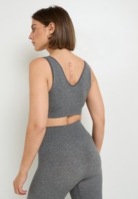 Reggiseno sportivo grigio a coste con spalline larghe e design a V sul retro, abbinato a leggings a vita alta coordinati. Texture liscia e forma aderente.