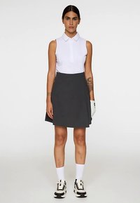 Polo bianca senza maniche con colletto, abbinata a una gonna a portafoglio grigio scuro. Calzini bianchi e sneaker bianche e nere completano il look.