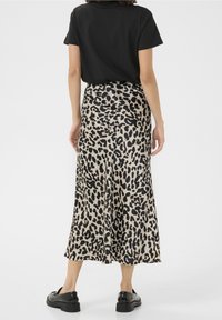 Midi sukně s leopardím potiskem a hladkým saténovým zakončením. Černý top a černé boty doplňují celý outfit. Neutrální pozadí.