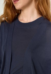 Haut tricoté texturé bleu marine avec un col rond et une ouverture devant. Les coutures améliorent la silhouette. Tissu doux et léger.