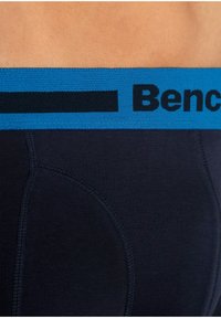 Marinefarbene Boxershorts mit einem blauen elastischen Bund, der schwarze Markenbeschriftung trägt. Der Stoff weist eine gerippte Textur und kontrastierende Nähte auf.