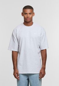 Gray short-sleeve t-shirt with a round neckline and subtle logo detail on the chest. Worn with light blue denim pants.