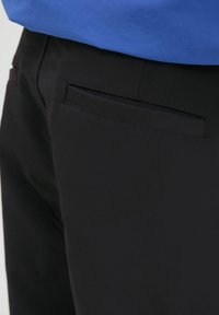 Pantaloni negri cu o textură netedă, având un singur buzunar la spate și accente cusute. Asortați cu un top albastru.