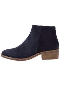 Botas náuticas de ante hasta el tobillo con un diseño elegante, punta redondeada y un tacón bajo apilado. Presenta un detalle de costura clara en contraste.