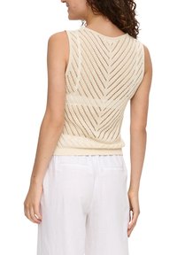 Lichtbeige gebreide tanktop met een zigzagpatroon en ribbelzoom. Open geweven ontwerp. Gecombineerd met witte, losse linnen broek.
