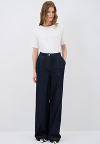 Valkoinen lyhythihainen paita punaisilla kaulustiedoilla; korkeavyötäröiset tummansiniset farkkujen leveät lahkeet etutaskuilla ja hopealla napilla.