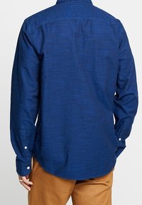 Mörkblå långärmad skjorta med texturerad tyg, knappade ärmslut, lätt svängd fåll och en ren ryggdesign.