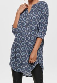 Camicia tunica a maniche lunghe con motivo floreale blu, patta dei bottoni, orlo arrotondato e una sottile texture lucida del tessuto.