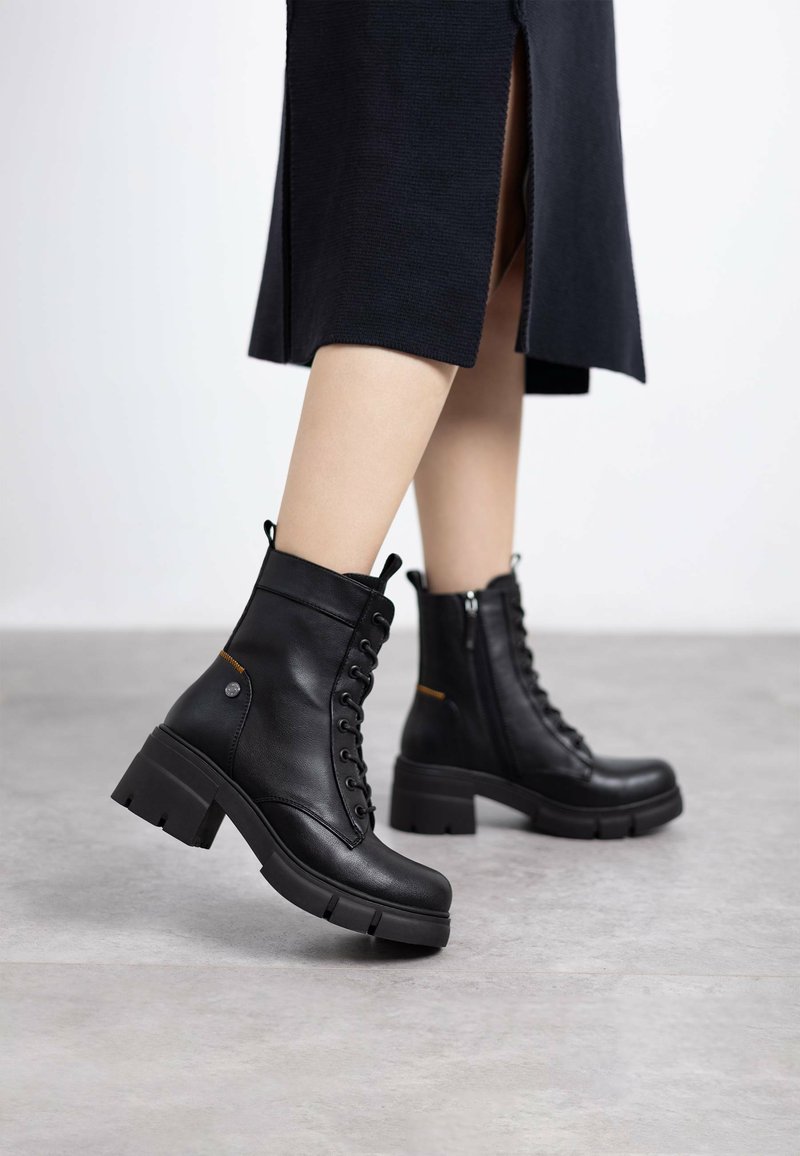 Botas de tobillo de cuero negro con tacón grueso, cordones en el frente y cremallera lateral. Presentan un material texturizado y acentos en contraste.