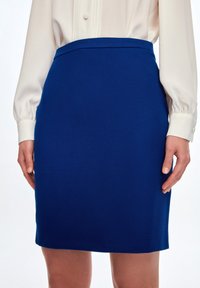 Blå blyertskjol med en slät textur, hög midja och knälång design. Matchas med en krämfärgad blus med långa ärmar.