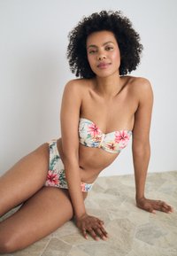 Blomstrete bikinitrøye med stroppeløst, polstret topp med tvistdetalj og matchende høyt liv-bukser; fargene inkluderer krem, rosa og grønn.