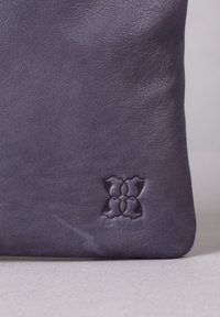 Dark purple leather bag with a smooth texture and embossed decorative pattern. Minimalist design, featuring rounded corners and subtle sheen.