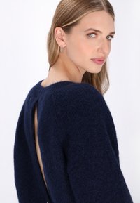 Dunkelblauer Pullover aus strukturiertem, fuzzy Strick, mit weitem Ausschnitt und offenem Rücken. Lange Ärmel mit lockerer Passform.