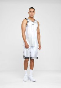Hvid atletisk tanktop og shorts med sorte lodrette striber. Har en rund hals og kontrasterende kant; bæres med hvide sneakers.