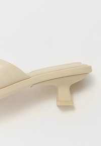 Sandale à talon beige avec une tige en simili cuir lisse, un design à bout ouvert, et un talon bloc qui se rétrécit en une base carrée.