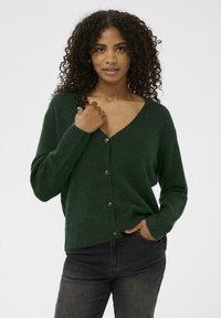 Cardigan verde tricotat cu decolteu în V, mâneci lungi și închidere cu cinci butoane. Prezintă mansete și tiv cu rigiditate, textură moale.