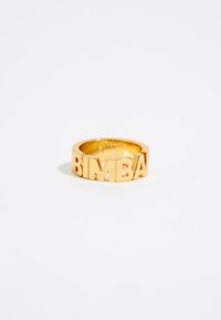 Anello in tono oro con la parola "BIMBA" in lettere ritagliate, banda arrotondata, finitura lucida, texture liscia e senza ulteriori abbellimenti.