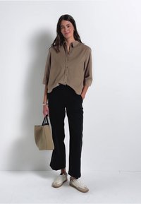 Chemise boutonnée marron clair, pantalons noirs à jambes larges, sac fourre-tout beige et baskets blanches. Design simple, tissu lisse et coupe décontractée.