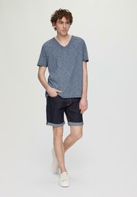 Niebieski melanżowy T-shirt z dekoltem w kształcie litery V, zestawiony z ciemnymi dżinsowymi szortami z podwiniętymi rękawami i białymi butami sportowymi. Prosty i swobodny design.