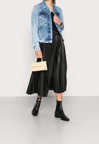 Denim jacket in light blue, pleated black leather midi skirt, black ankle boots with a chunky heel, and a small cream handbag.