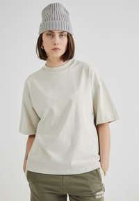 Tricou din bumbac de culoare gri deschis, supradimensionat, cu mâneci scurte și decolteu rotund, asortat cu pantaloni de culoare verde măsliniu. Design simplu, textură moale.