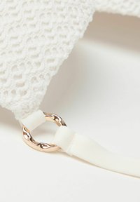 Bolso de tela blanca texturizada con un patrón tejido, que cuenta con un anillo de metal dorado y una correa blanca lisa.