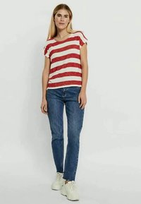 T-shirt de manga curta às riscas vermelhas e brancas combinado com jeans azuis e sapatilhas brancas. A t-shirt possui um decote redondo e um corte descontraído.