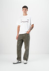 White t-shirt with "Functional Aesthetics" text, paired with olive-green textured pants and white sneakers with black accents.