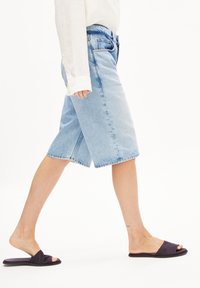 Vaaleansiniset farkku-bermudashortsit rentolla istuvuudella, käännetyillä lahkeensuilla ja viiden taskun mallilla. Yhdistetty tummiin liukuvaan sandaaleihin.