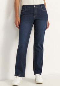 Mörkblå denimjeans med rak bendesign, med kontrasterande sömmar, framfickor och knappstängning. Matchas med vita sneakers.