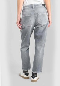 Jeans de mezclilla gris con un corte relajado, que cuentan con dos bolsillos traseros y detalles bordados. Las piernas se ajustan ligeramente en el tobillo.