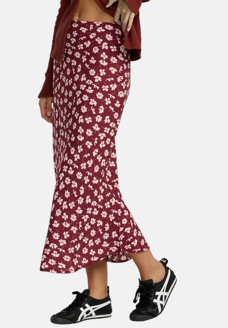 Gonna floreale bordeaux con un design svasato. Presenta piccoli fiori bianchi e rosa sul tessuto. Indossata con scarpe da ginnastica nere.